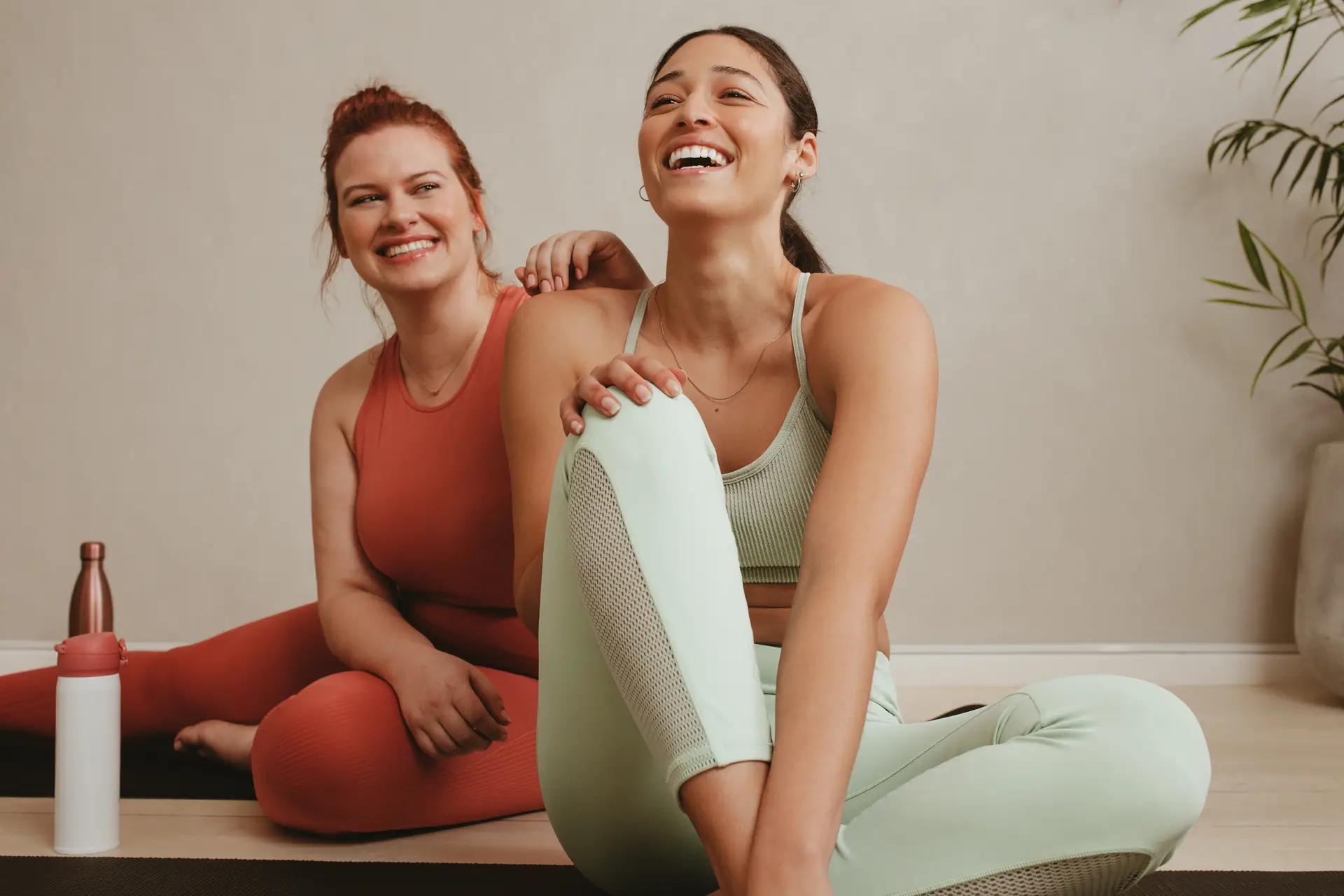 Two friends taking a break on the gym floor, discussing effective exercises for women.