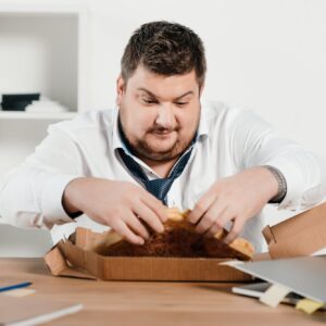 fat businessman eating pizza for lunch at workplace