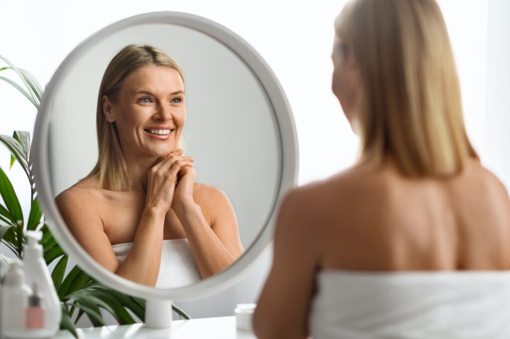 Skin Rejuvenation. Beautiful Mature Woman Looking In Mirror At her Reflection