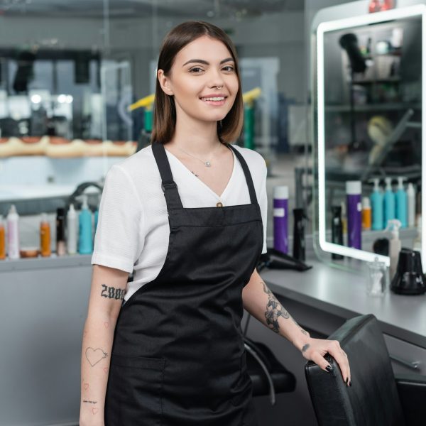 professional-headshots-tattooed-beauty-worker-in-apron-looking-at-camera-in-beauty-salon-.jpg